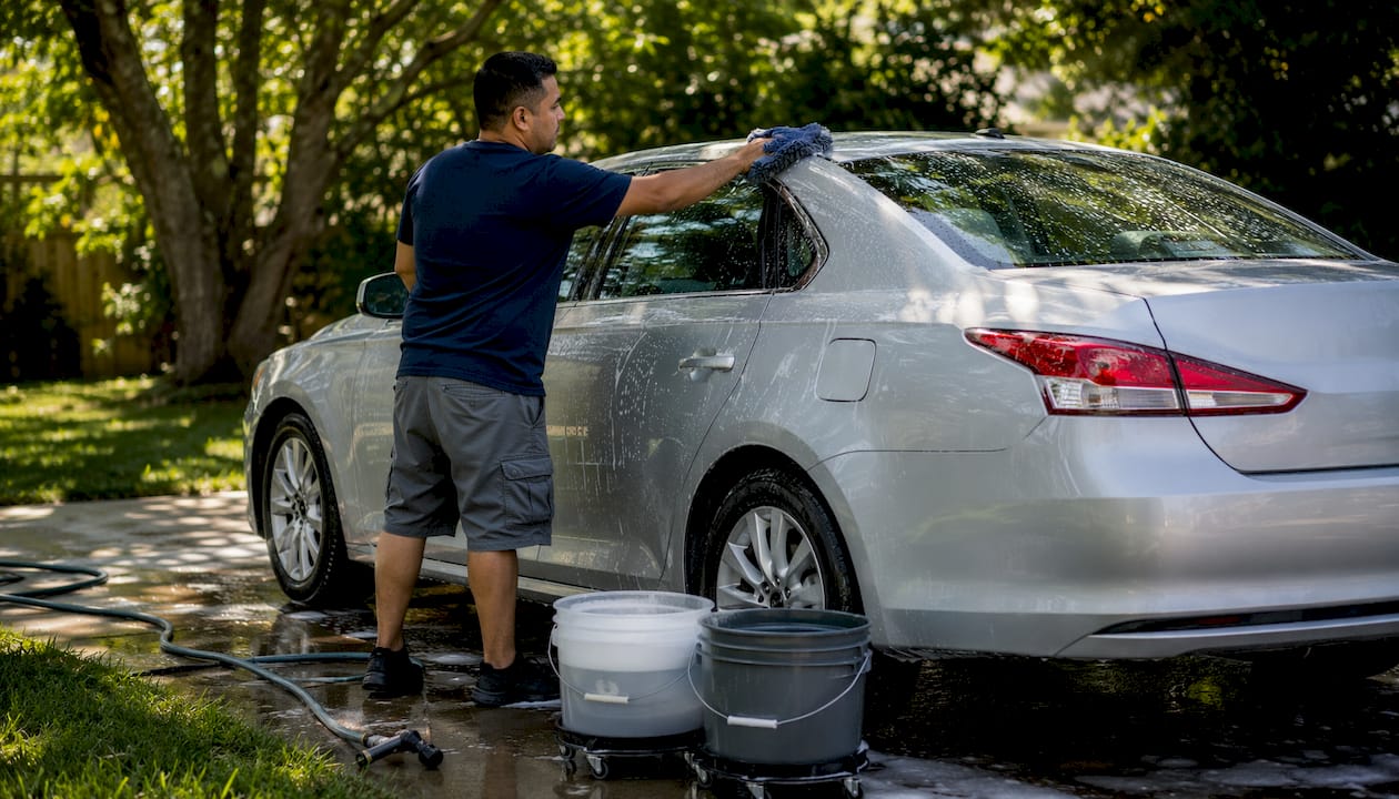 Man washing car with two-bucket method in driveway