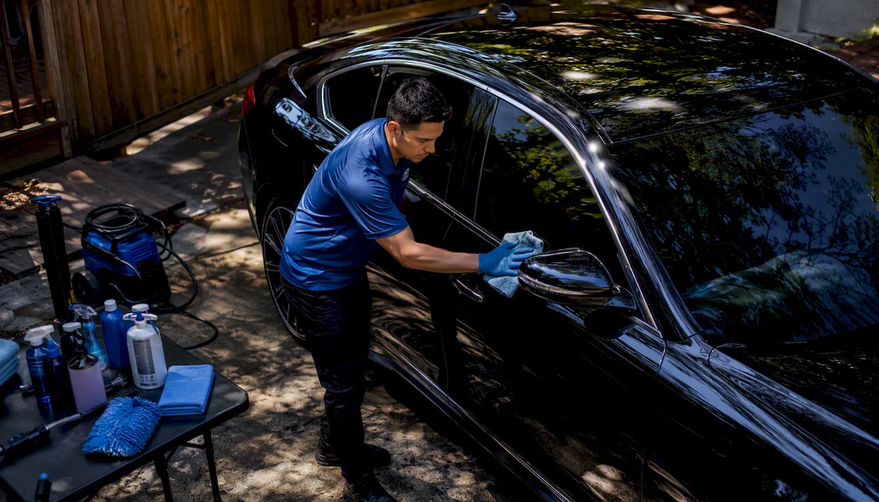 Mobile car detailer cleaning black sedan outdoors