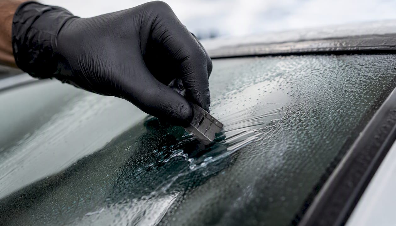 Hand using razor blade on car window