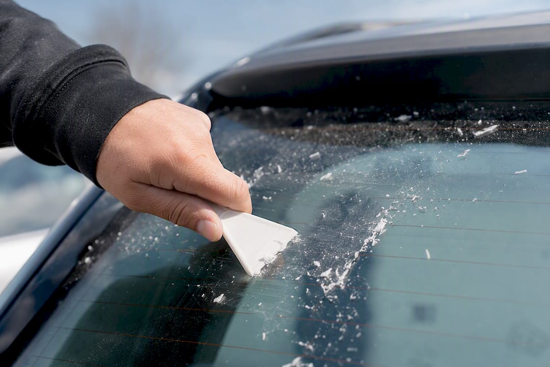 Plastic scraper removing adhesive on rear window glass